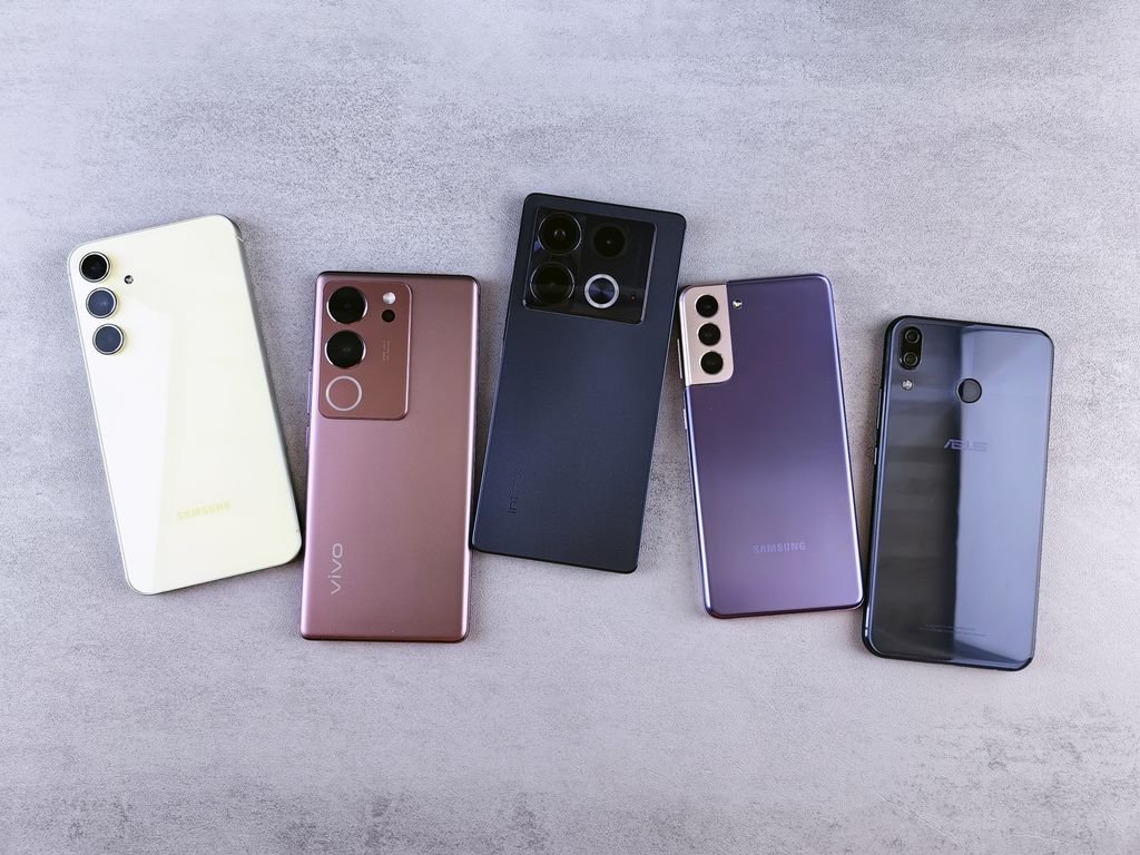 Cinco novos smartphones lado a lado sobre superfície cinza, mostrando designs variados dos lançamentos de 2026